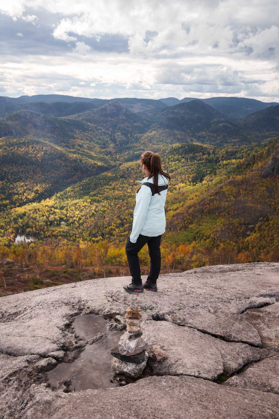 A person in hiking clothes looks over the Charlevoix landscape from the top of a rocky rest stop.