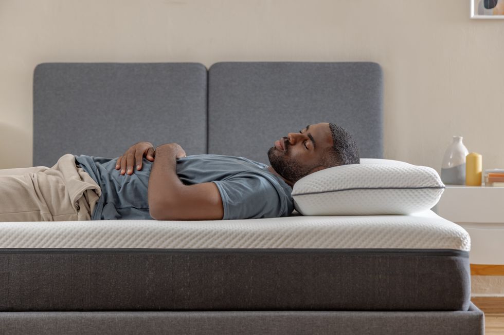 A person lays on their back on an Emma mattress, sleeping with their head on a pillow and hands resting on their stomach.