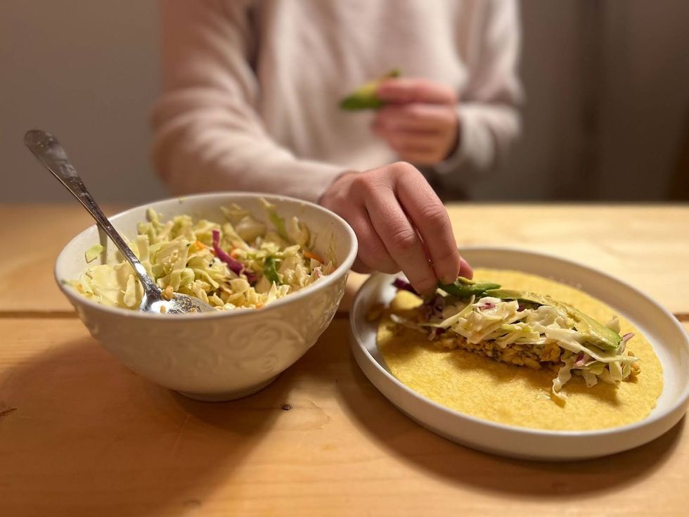 A person lays slices of avocado onto the filling of a fish taco.