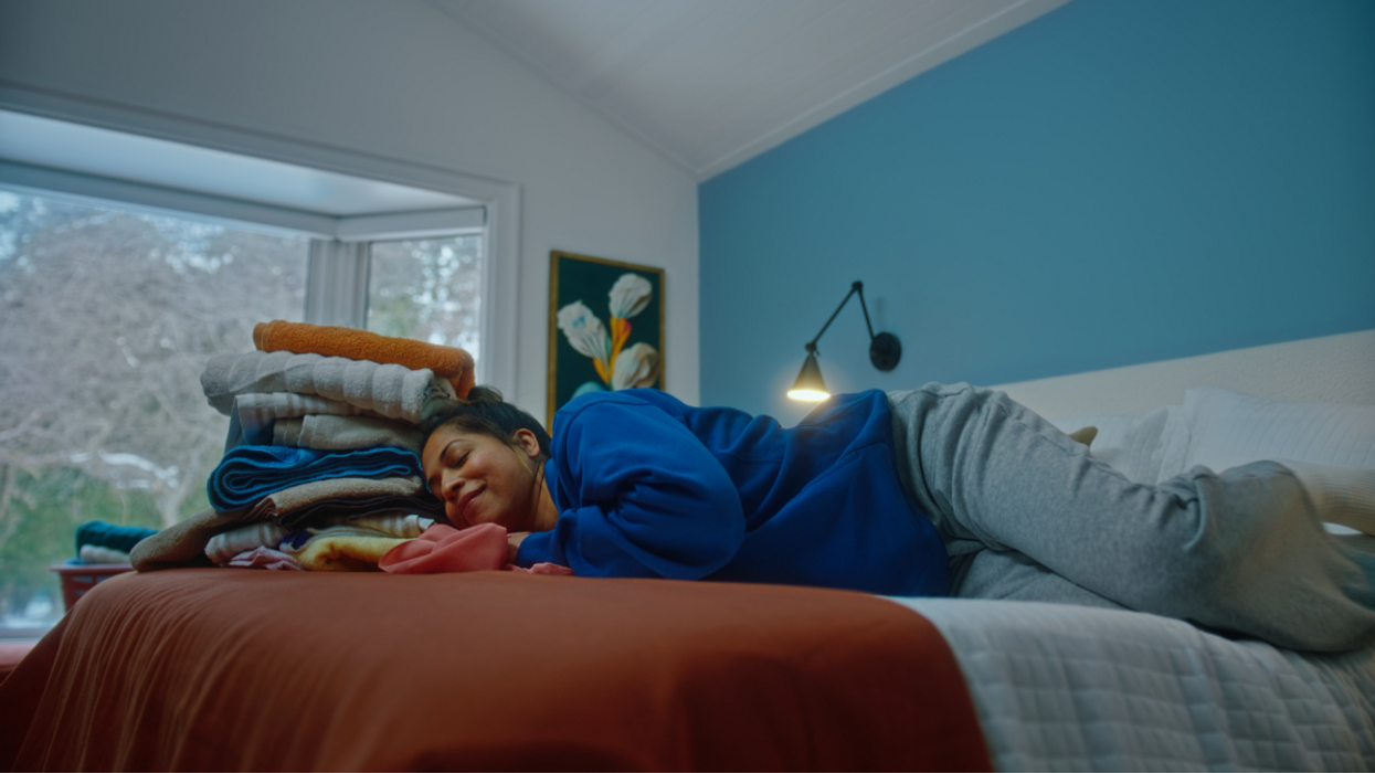 A person naps on a bed covered with freshly folded laundry.