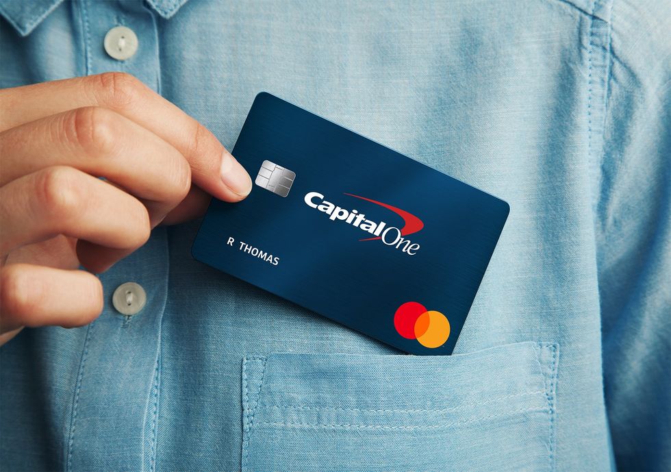 A person pulls a Capital One credit car out of their shirt pocket.