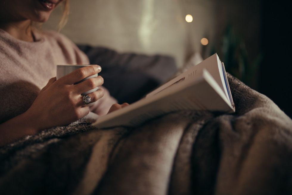 A person reading in bed with a cup of tea.
