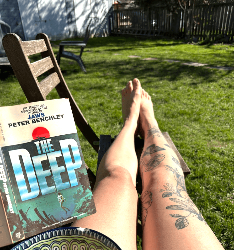 A person relaxing outside, reading a book with their feet up.