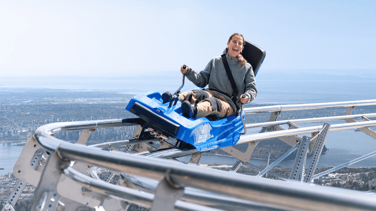 A person rides the Grouse Gravity Coaster with the Vancouver skyline in the background.
