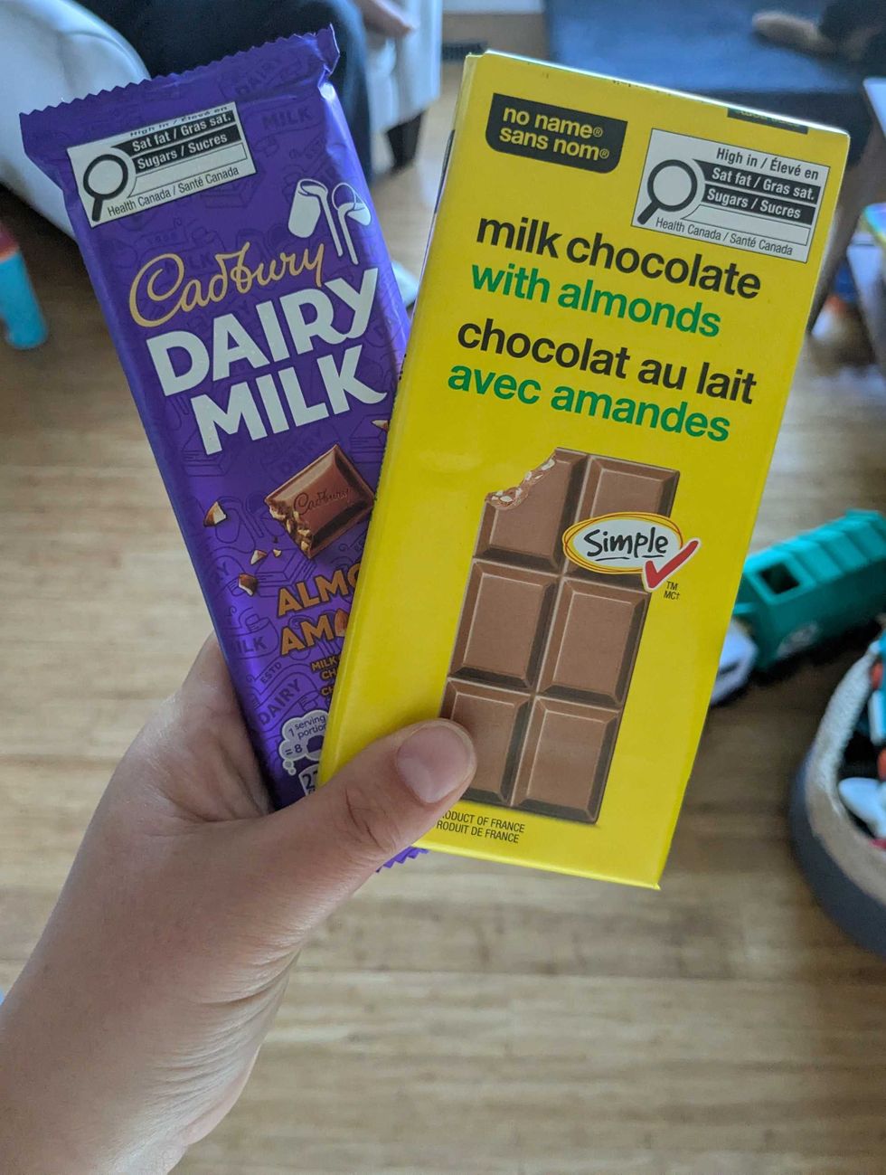 A person's hand holding a Cadbury's and No Name chocolate bar