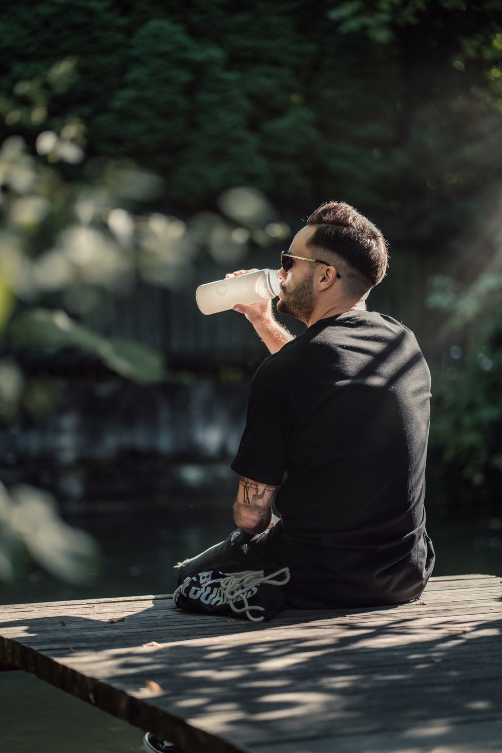 A person sits on the edge of a dock and drinks water from a bottle.