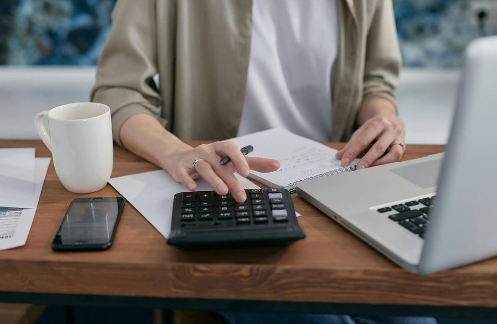 A person sitting at a desk with a laptop using a calculator.