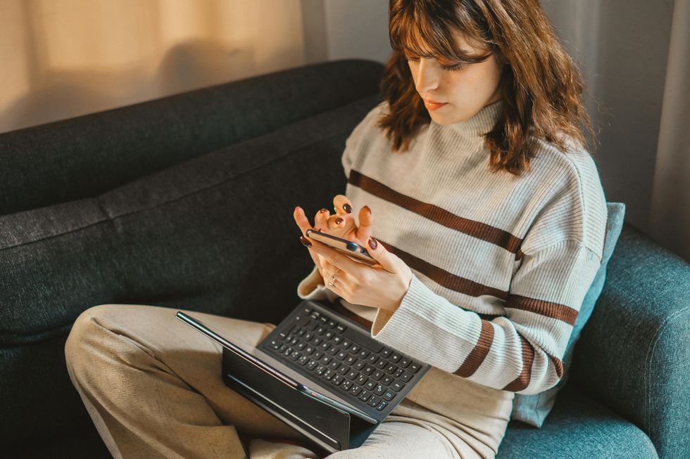 A person sitting on the couch with a laptop browsing something on their phone.