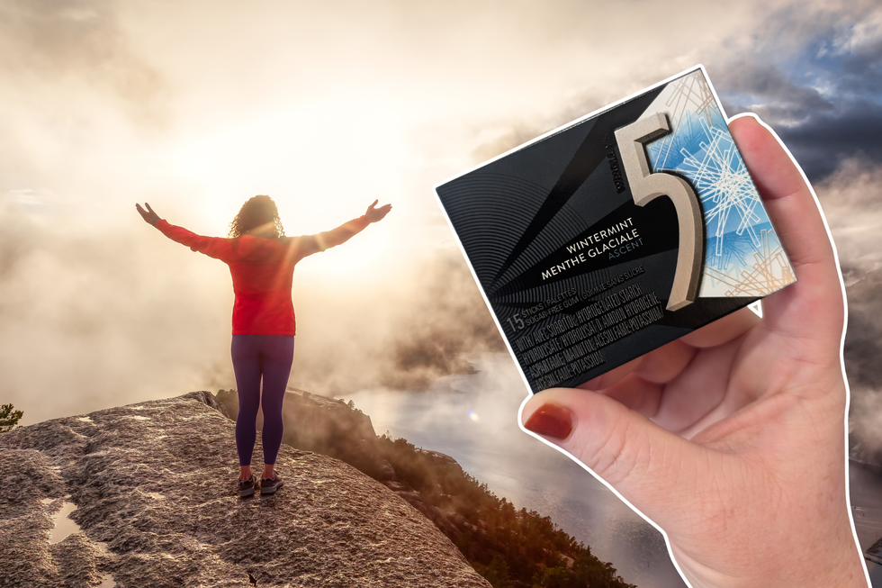 A person standing on top of a mountain with their arms outstretched overlooking a lake. A hand holding Ascent flavour 5 Gum is on top.
