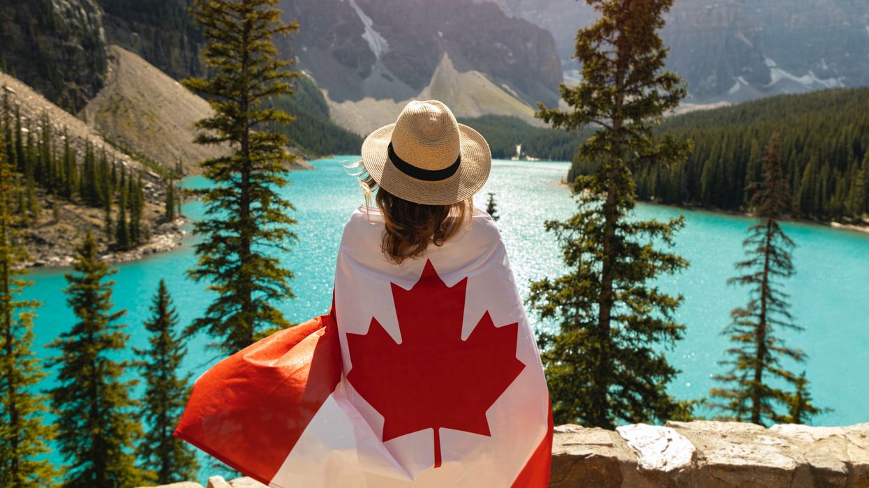 A person stands draped in a Canadian flag in front of a blue lake.