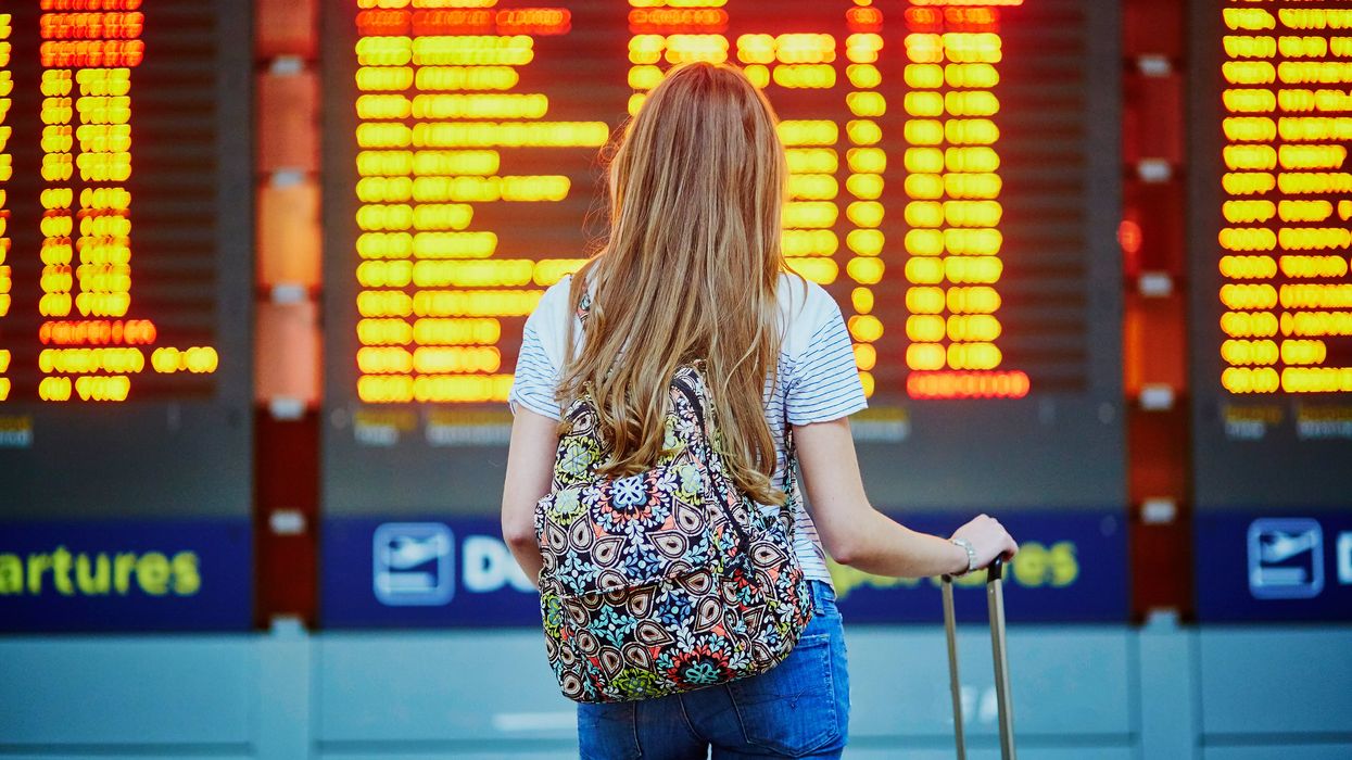 A person stands in front of a flight information board at an airport.