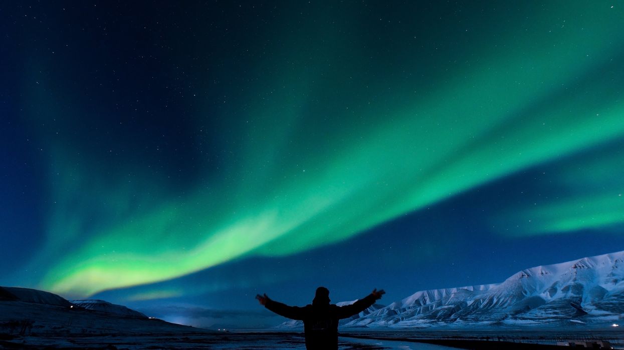 A person stands under the northern lights.