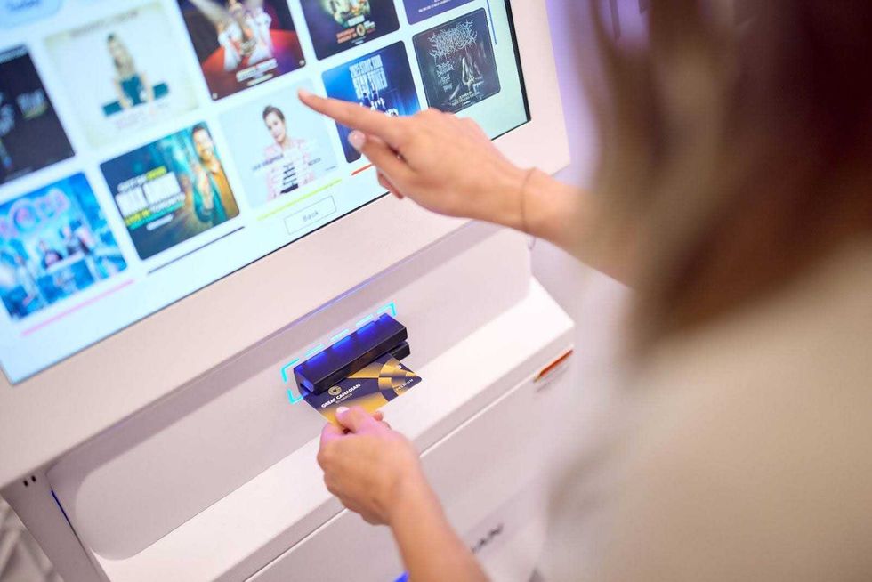 A person swipes their Great Canadian Rewards card at a white kiosk and selects a show from the touch screen.
