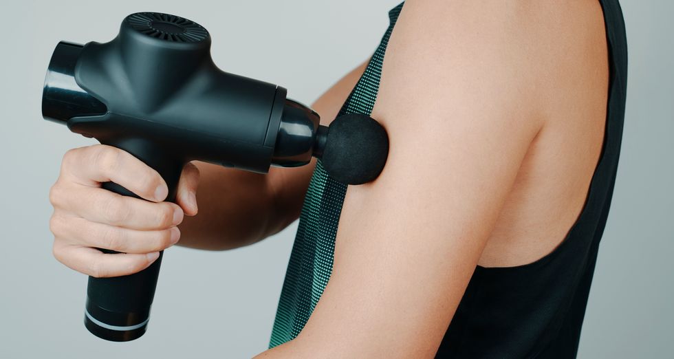 A person uses a percussive massage gun on their upper arm.