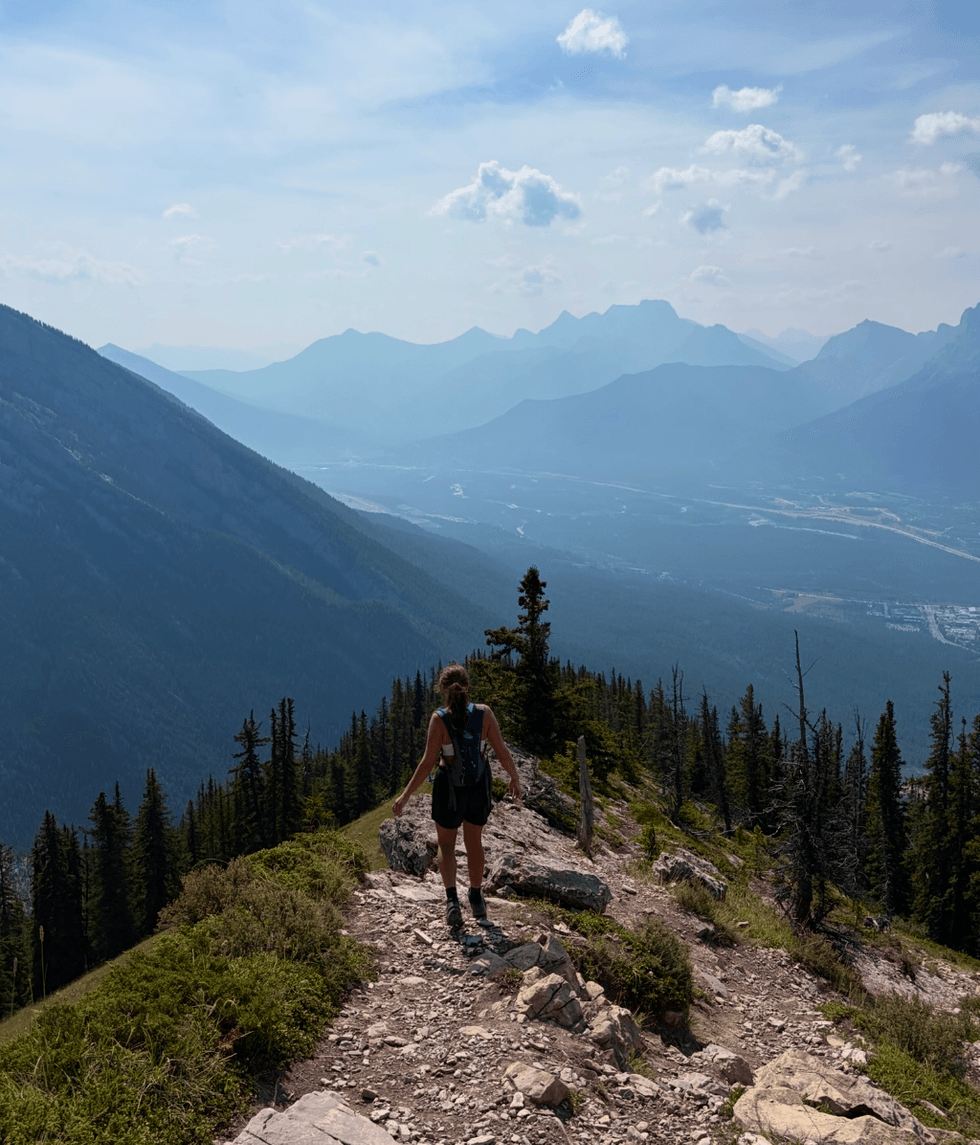 A person walking on a trail with a lookout of surrounding montains.