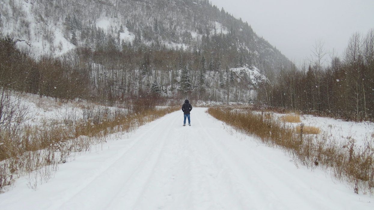A person walks on a snowy path with a snow-covered hill in the background.