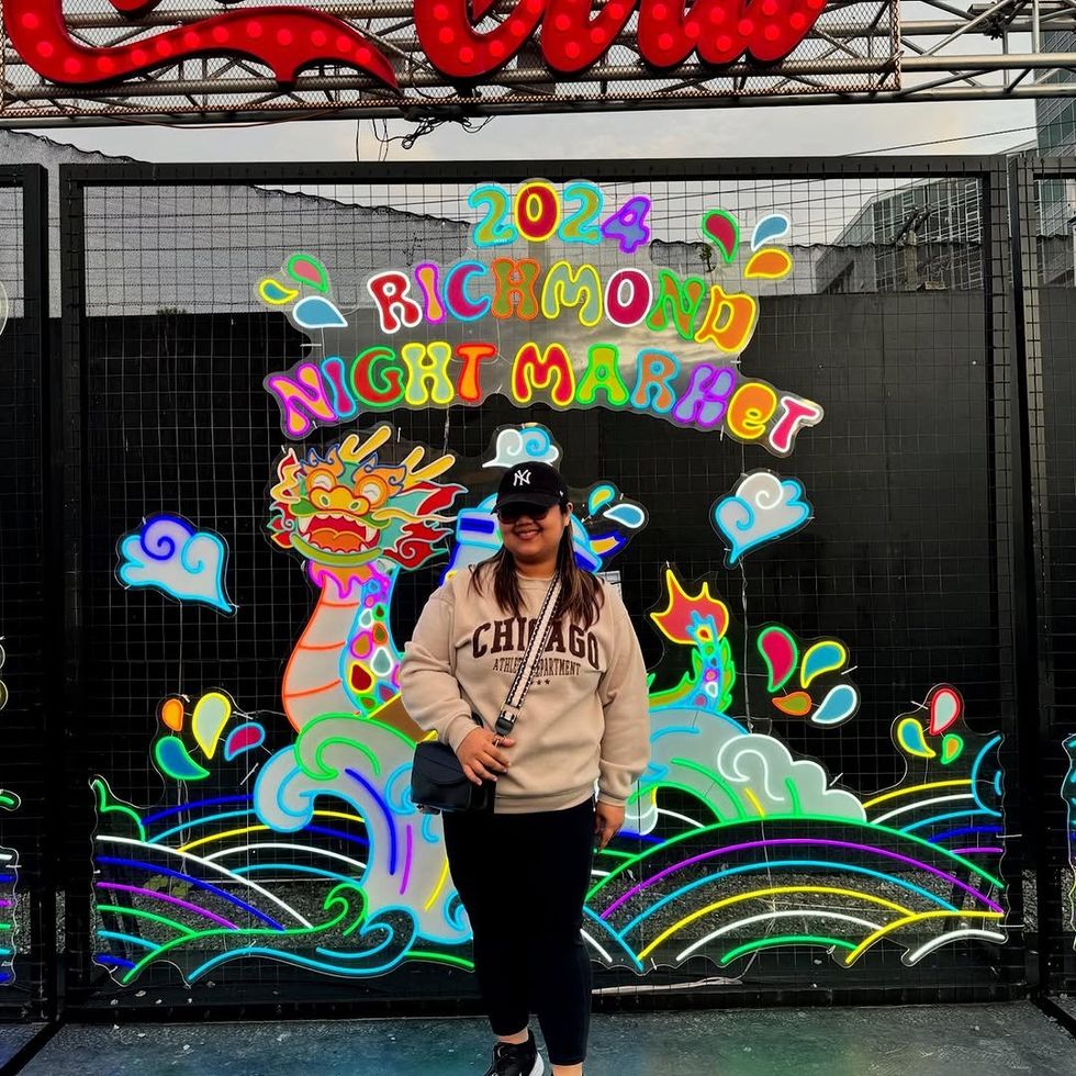 A person wearing Yankees baseball cap, light sweatshirt and sunglasses in front of a neon sign that reads "Richmond Night Market."