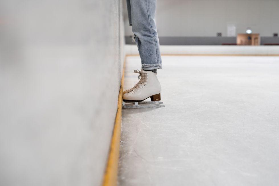 A person wears figure skates on the ice at an indoor skating rink.