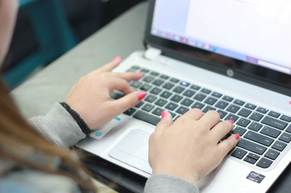 A person with pink nails types on the keyboard of a laptop computer.