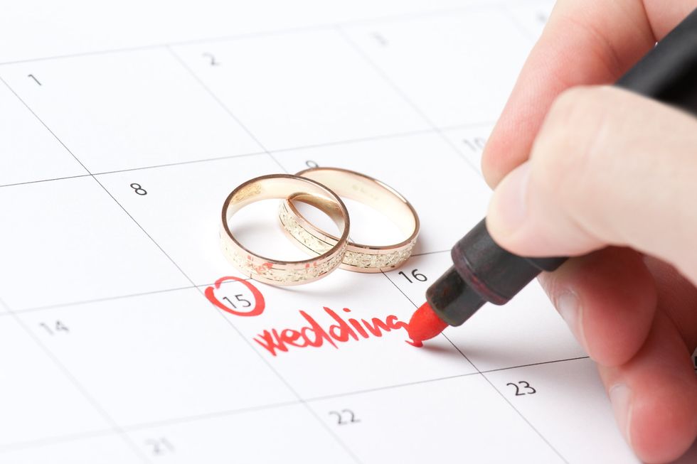A person writing "wedding" on their calendar. with two wedding bands next to it.