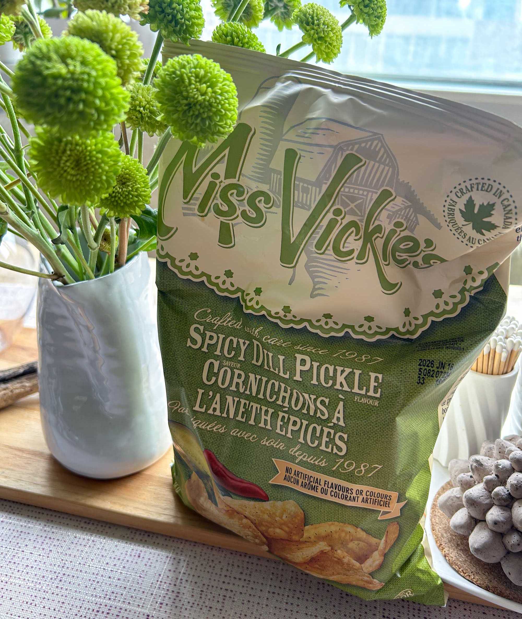 a photo of miss vickie's spicy dill pickle potato chips on a kitchen table next to fresh flowers