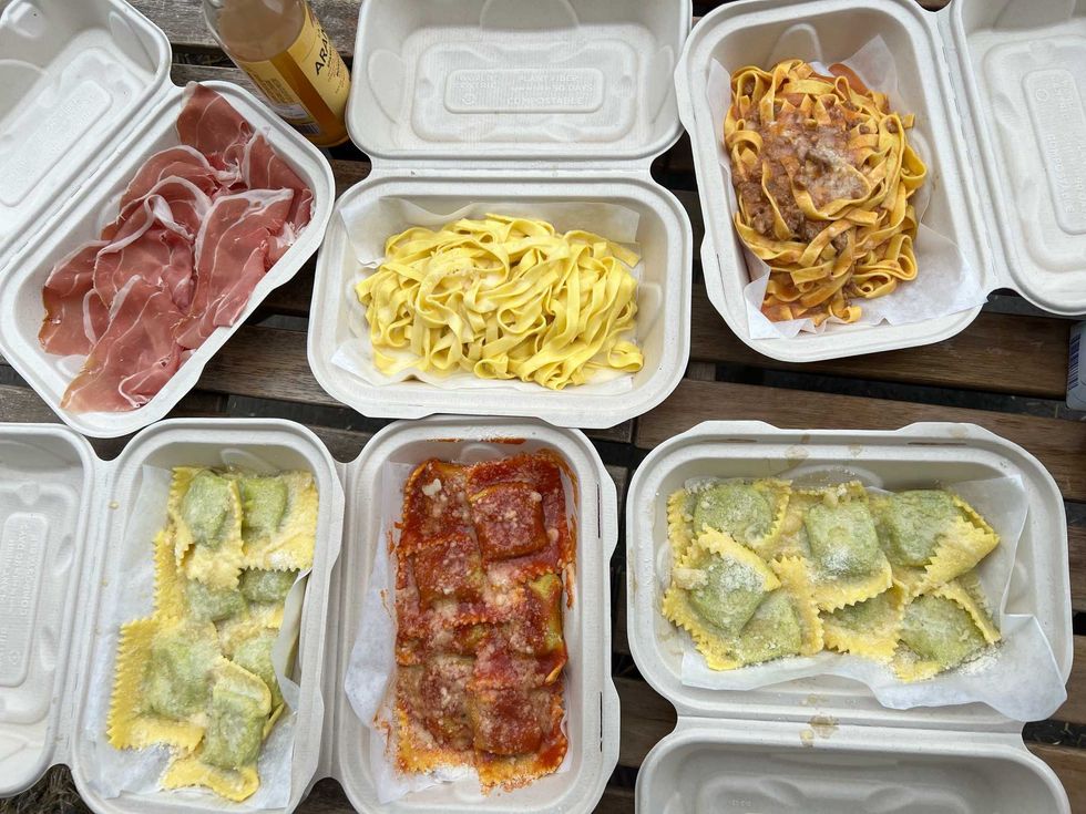 A picnic table full of takeout container pasta dishes and prosciutto