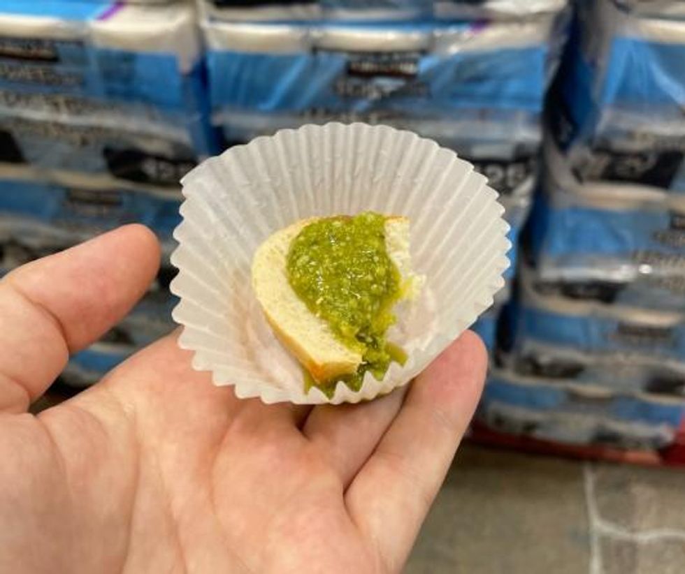 A piece of bread with pesto on it in a paper cup.