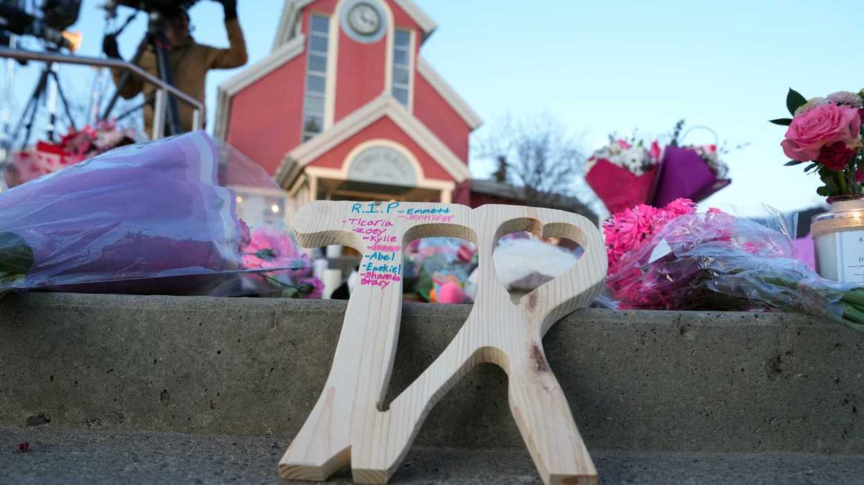 A piece of wood carved with "TR" with the names of victims on it is shown at a vigil for the victims of a mass shooting