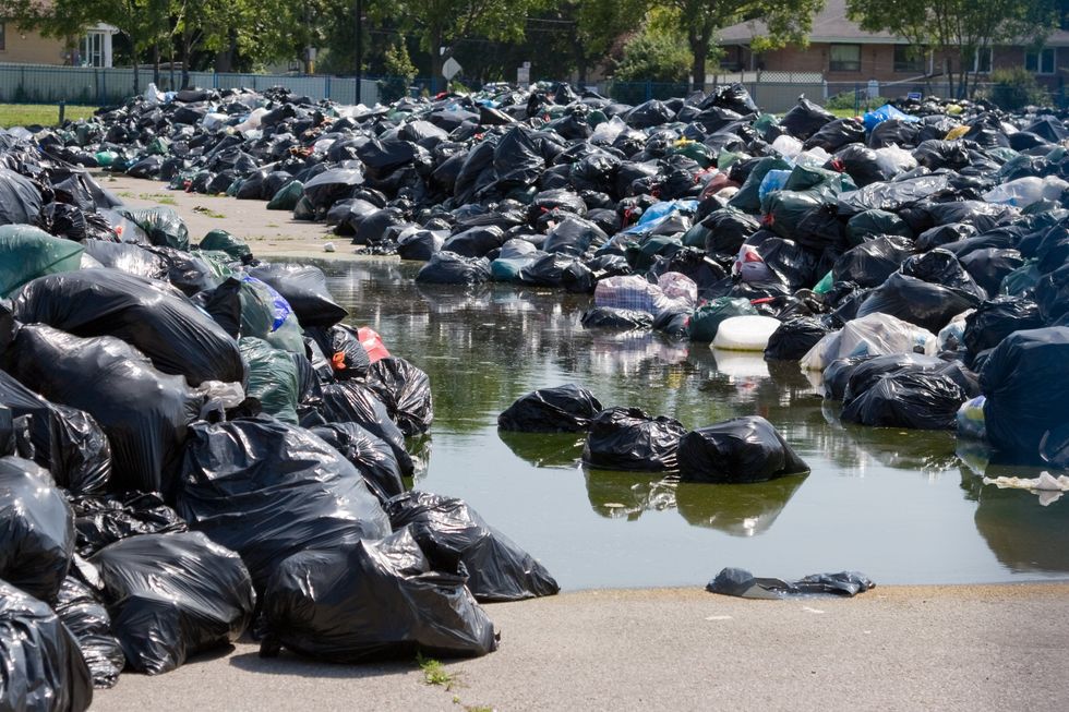 A pile of garbage bags piled up with some in the water.