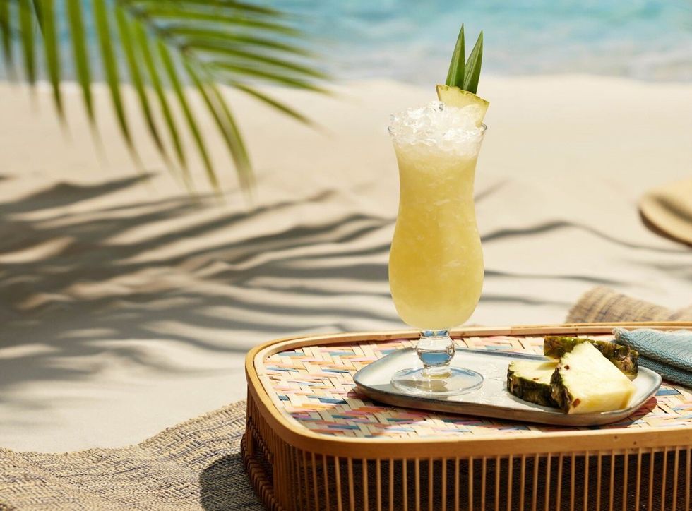 A pina colada on a tray by a beach.