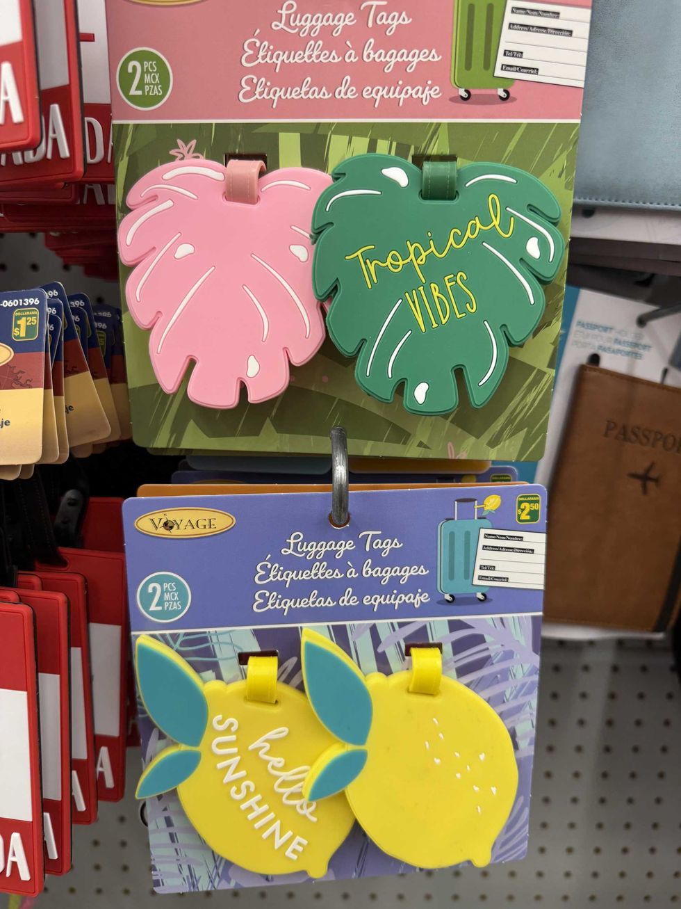 A pink and green leaf-shaped luggage tags hanging on a store shelf above two lemon shaped luggage tags.