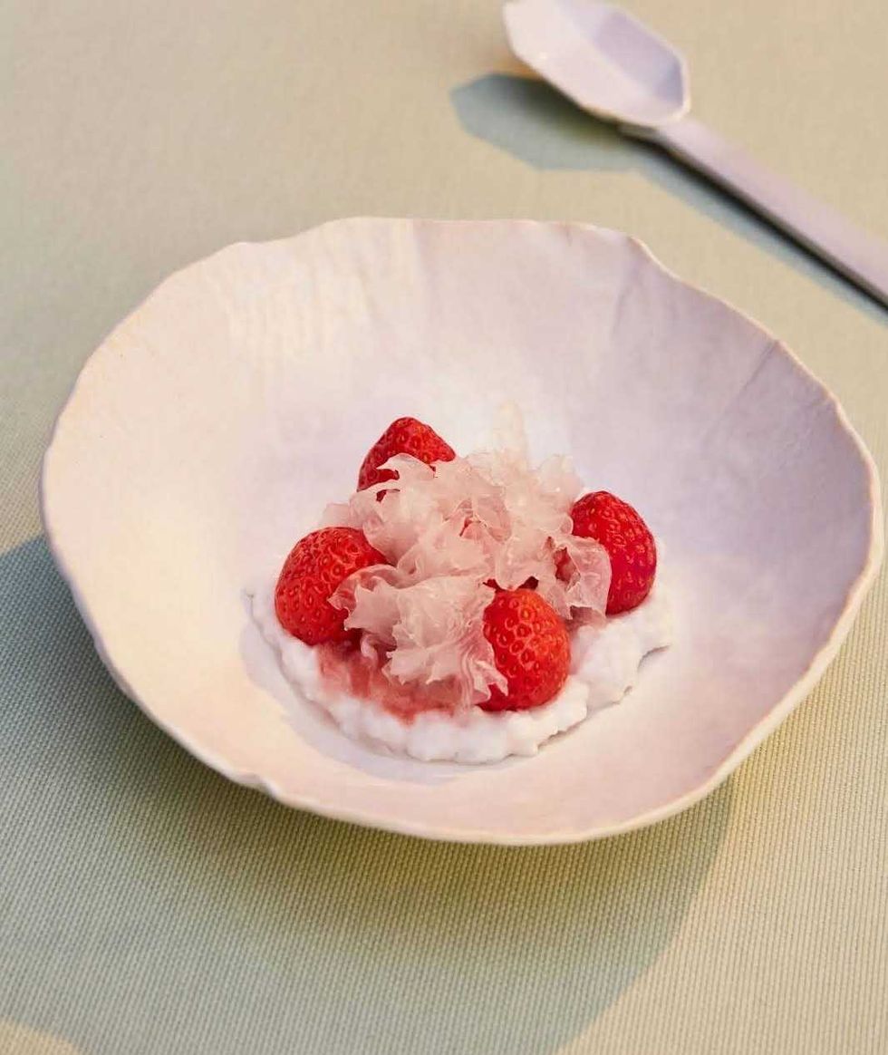 A pink bowl filled with rice pudding and topped with strawberries.