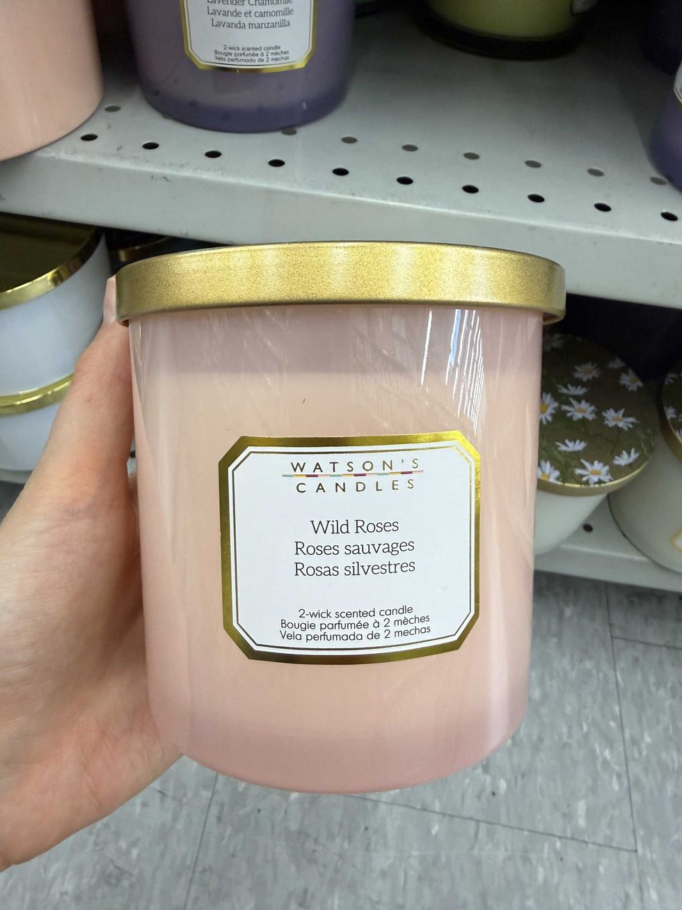 A pink glass container with a gold lid and a label reading Wild Roses 2-wick scented candle.