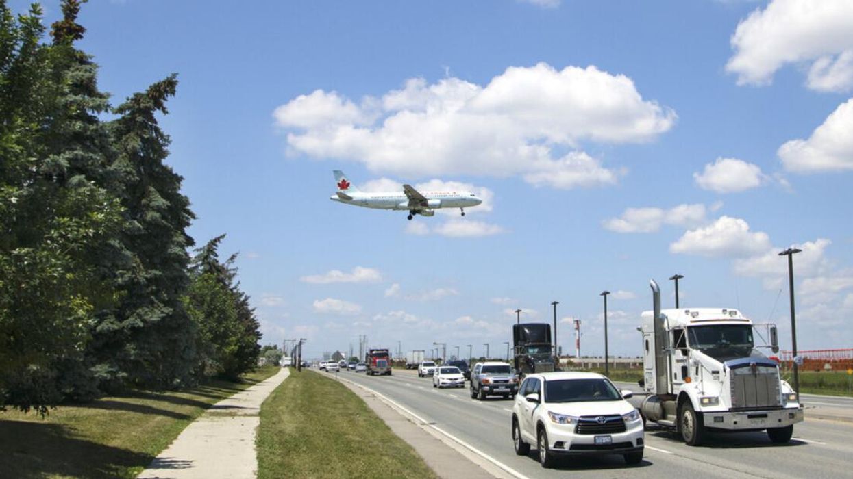 A plane flying over a busy street as it comes in for landing at Toronto Pearson Airport.