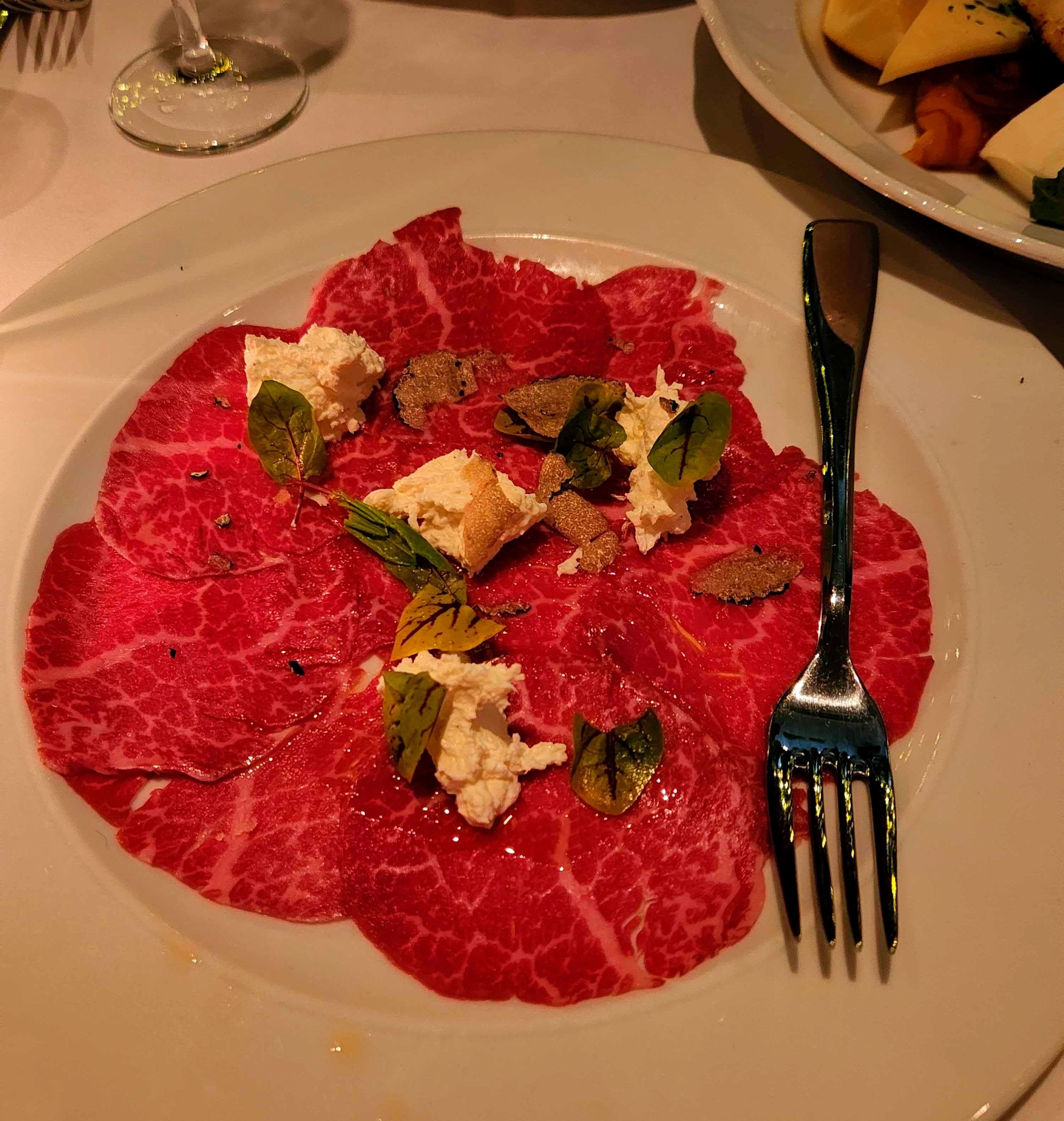 A plate of beef carpaccio from Sotto Sotto with a fork.