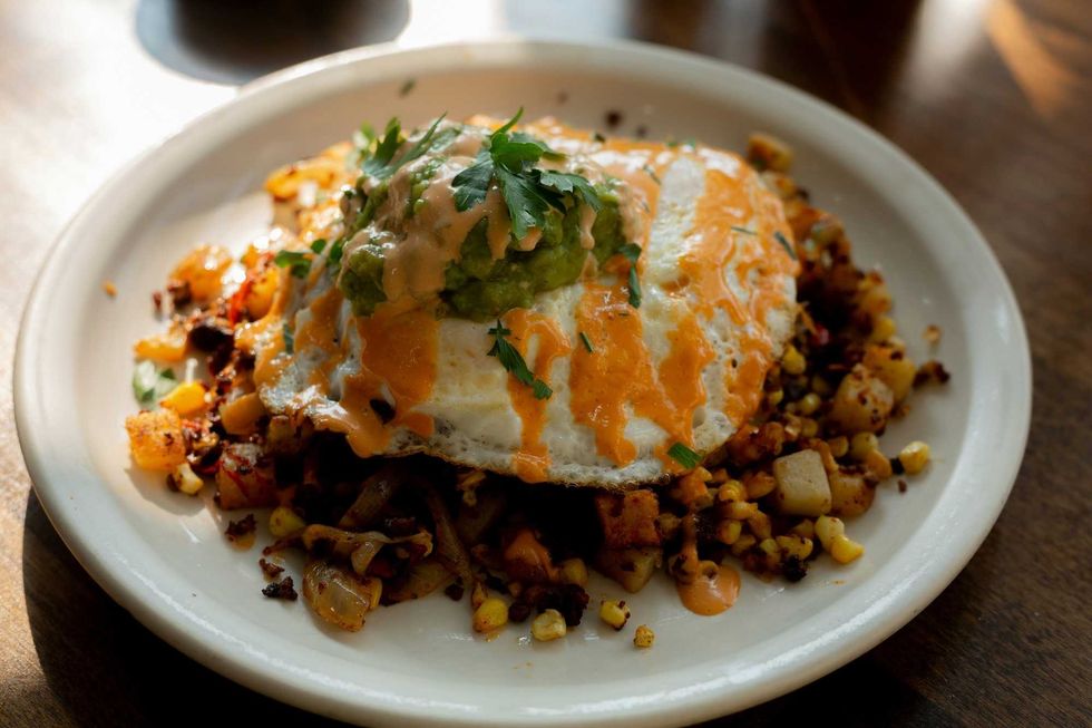 A plate of mixed breakfast vegetables topped with a fried egg, avocado and parsley.