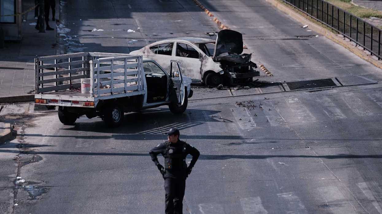 A police officer stands guard by a charred vehicle after it was set on fire, on a road in Guadalajara, Jalisco state, Mexico.
