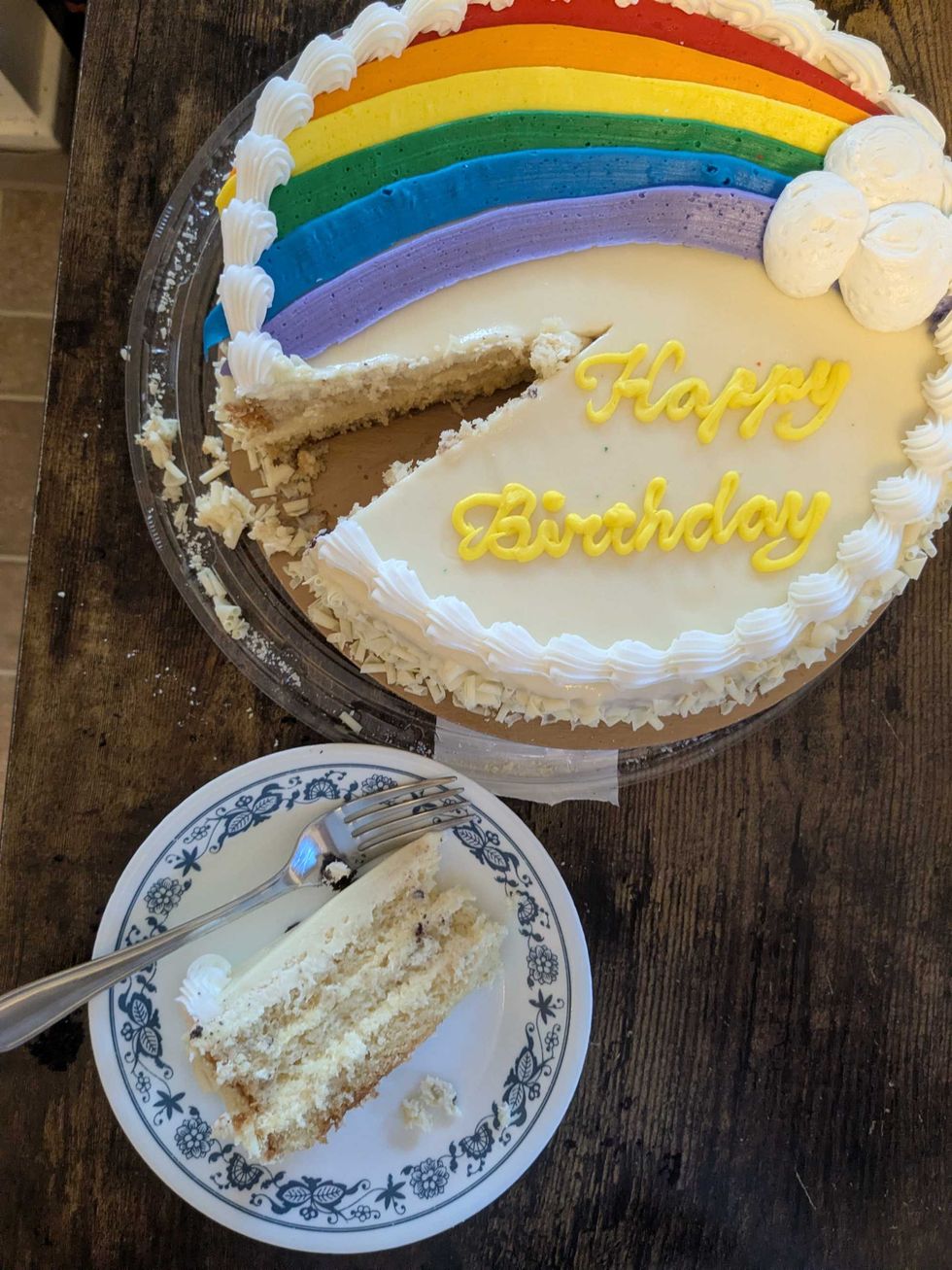 A rainbow cake with a slice taken out and on a plate next to it.