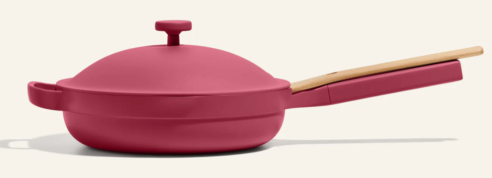 A raspberry coloured- cooking pan with a wooden spoon attached.