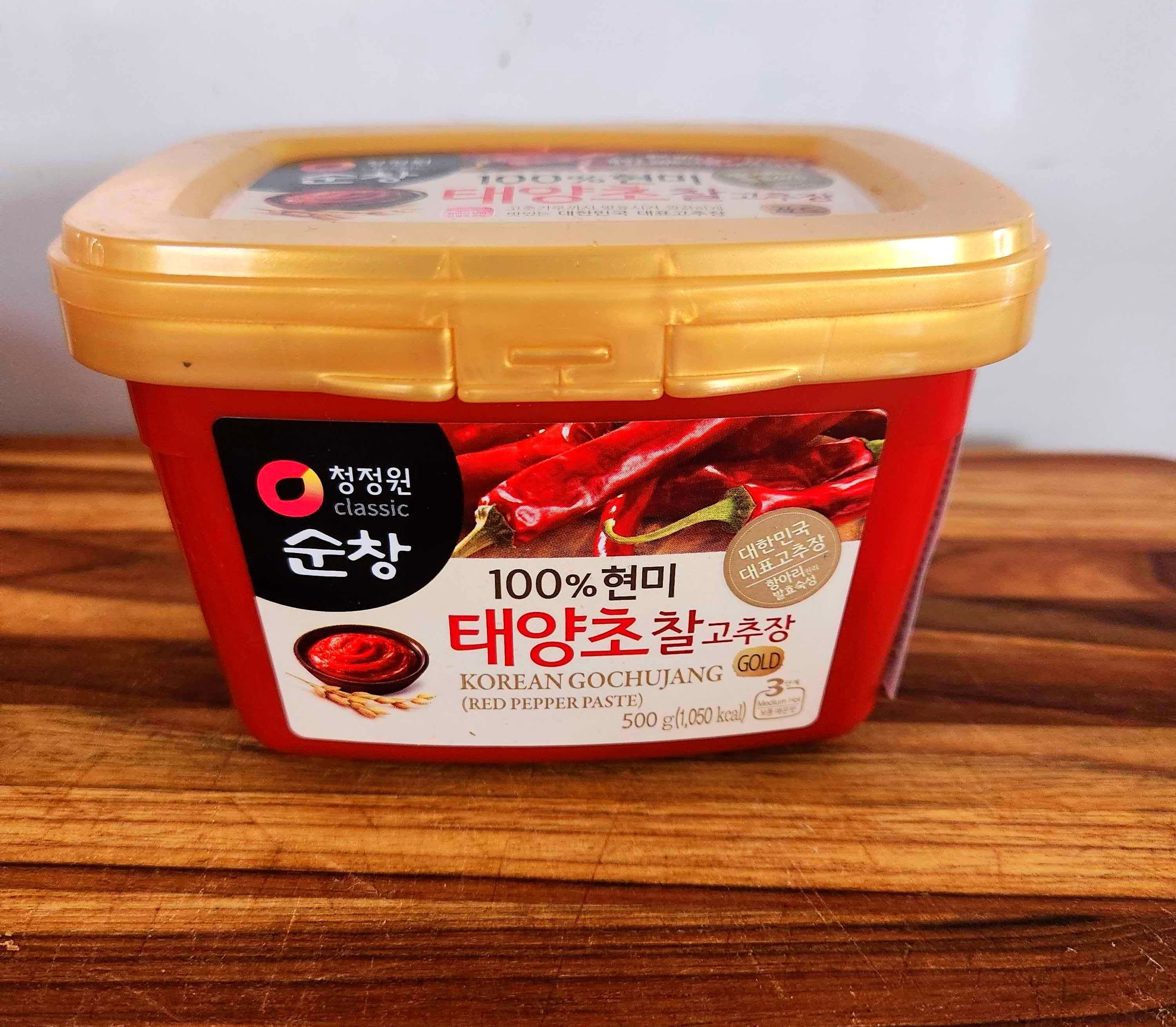 A red container with a yellow lid on a wood cutting board.