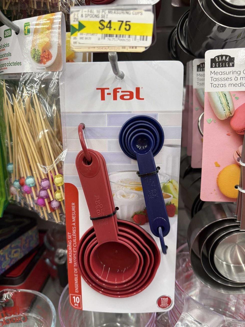 A red set of measuring cups and a blue set of measuring spoons hanging on a store shelf.