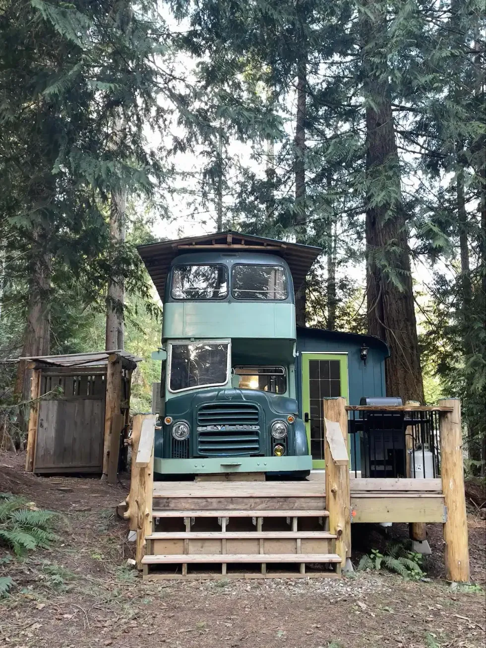 A refurbished teal bus with a deck in front with a BBQ on it.