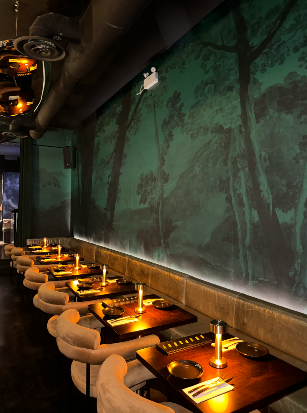 A room in a restaurant with green wallpaper and pink chairs.