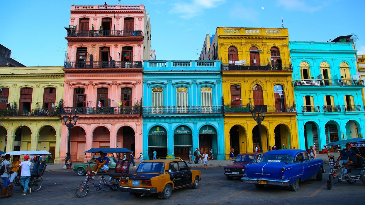 A row of brightly coloured houses with old cars parked outside in Cuba.