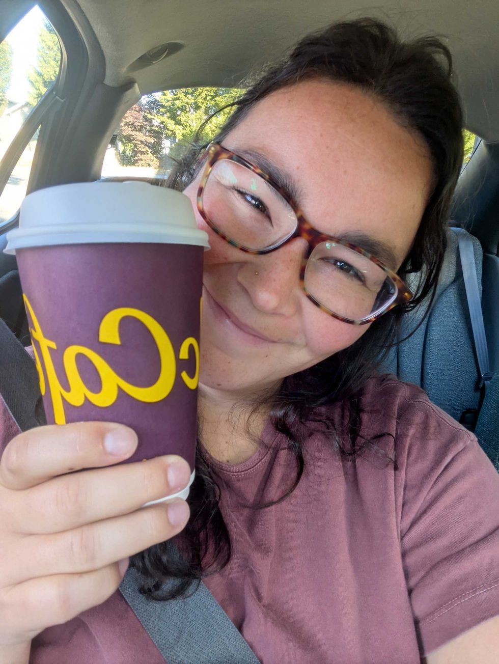 A selfie of a woman with dark hair and classes holding up a McDonald's coffee cup