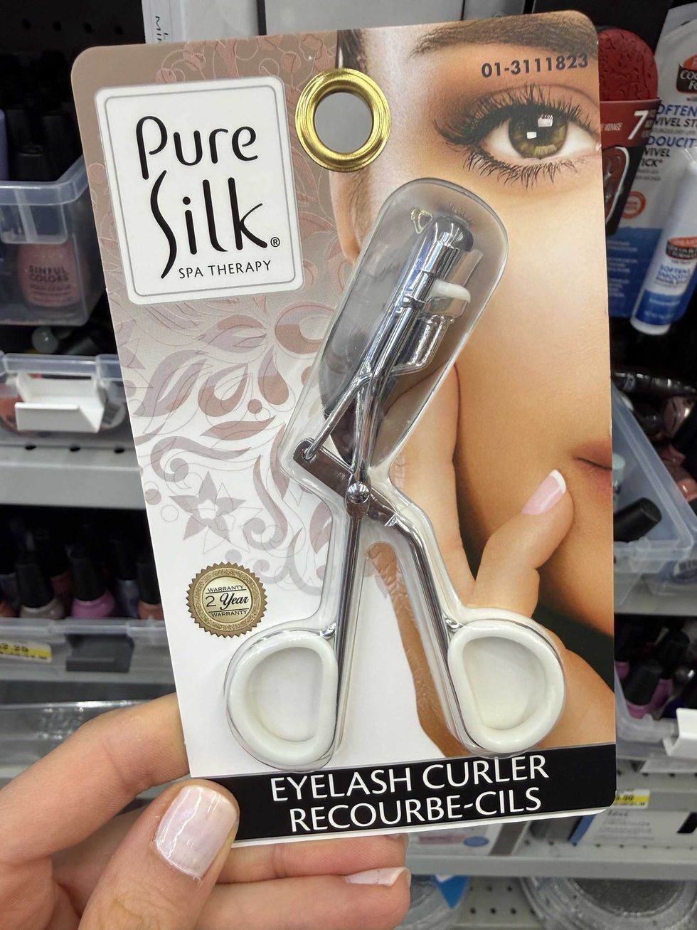 A silver and white eyelash curler with a picture of a woman's eye on the front.
