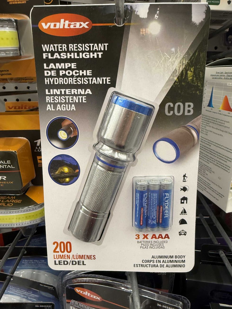 A silver flashlight with three batteries packaged together hanging on a store shelf.