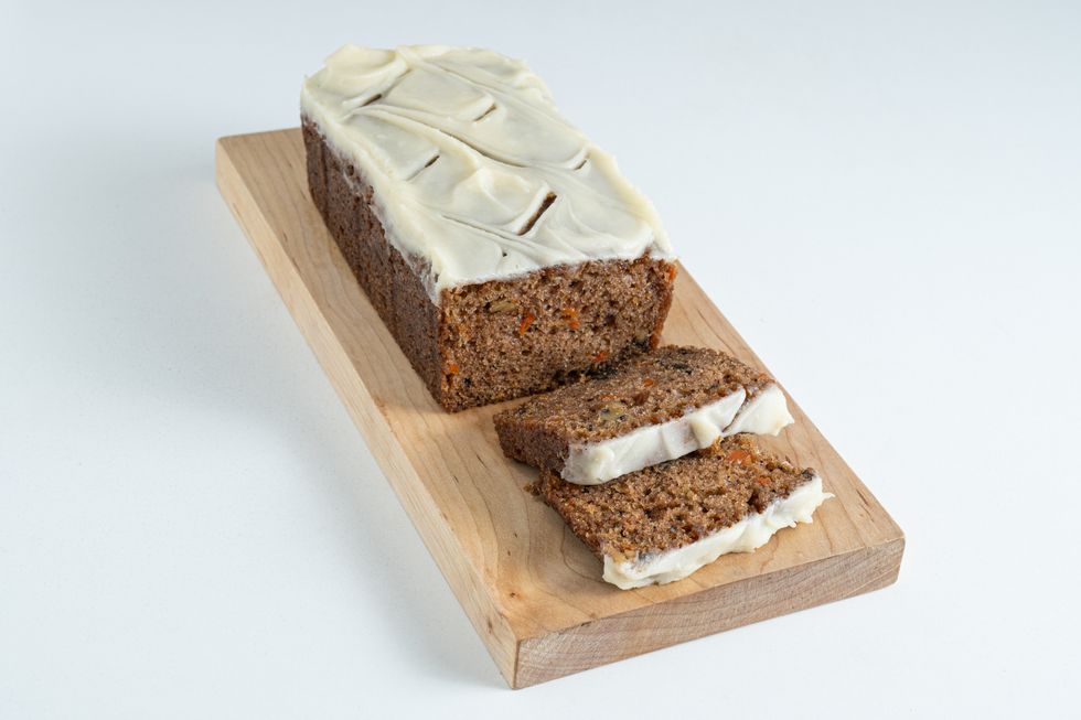 A sliced rectangular carrot cake with cream cheese frosting on a wood chopping board.