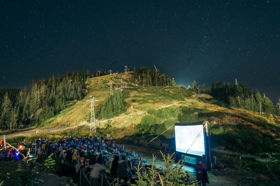 A small crowd watching an outdoor movie screen erected on the top of Grouse Mountain.