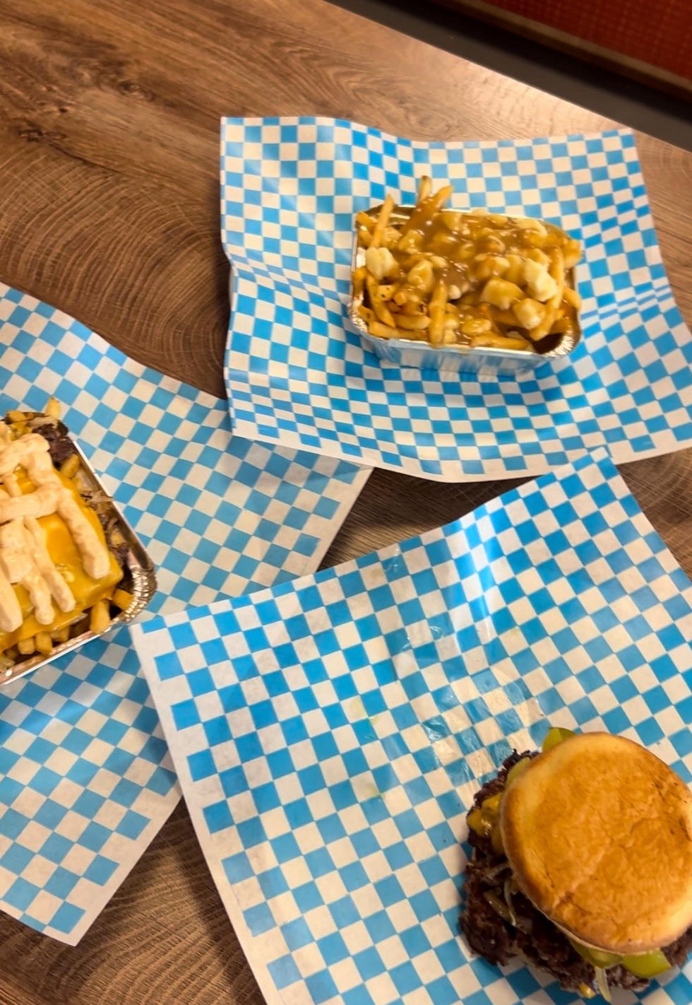 A smash burger, poutine and loaded fries in takeout paper.